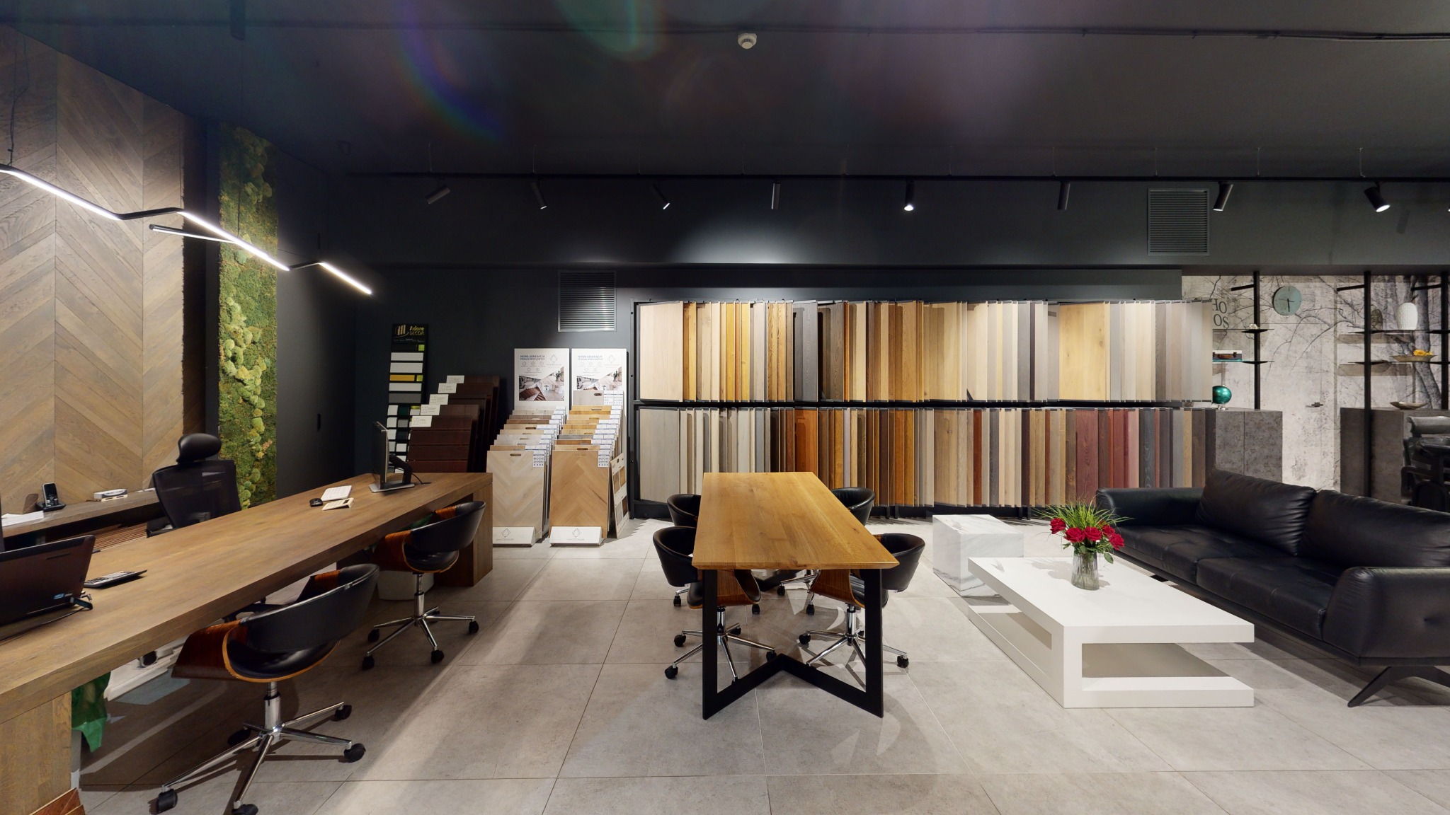 Salon z ekspozycją paneli podłogowych i parkietów, z długim drewnianym stołem, sofą i dekoracją z mchu na ścianie.