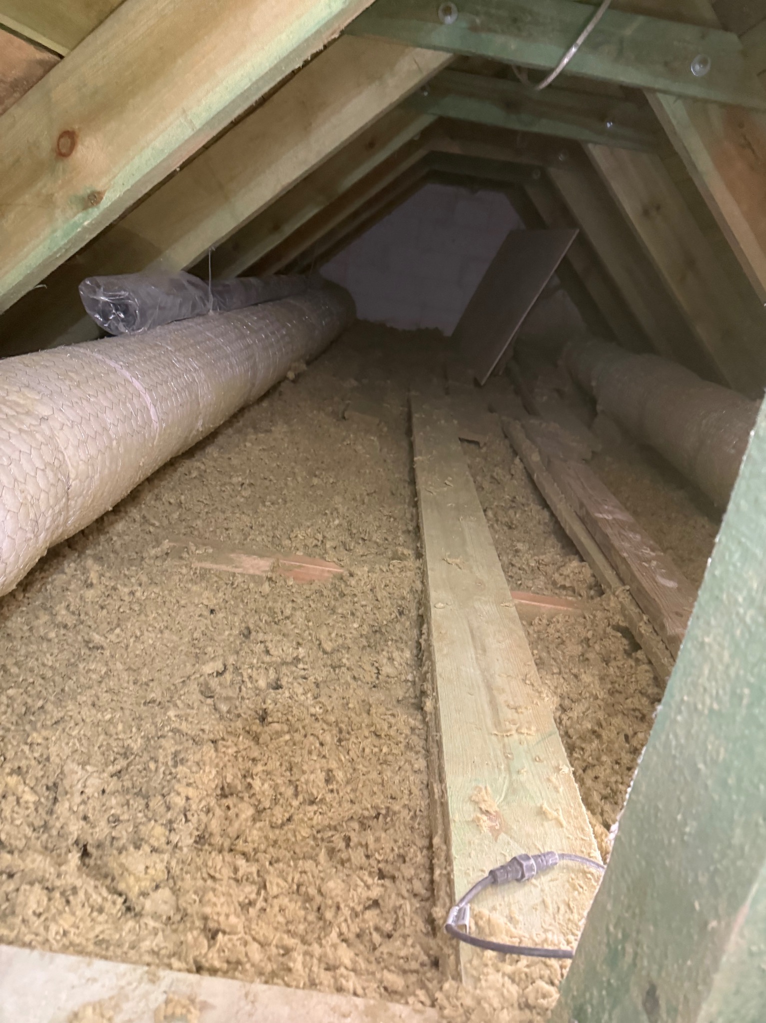 Poddasze wypełnione wełną mineralną, widoczne drewniane elementy konstrukcyjne i rura wentylacyjna. Izolacja termiczna w trudno dostępnej przestrzeni.