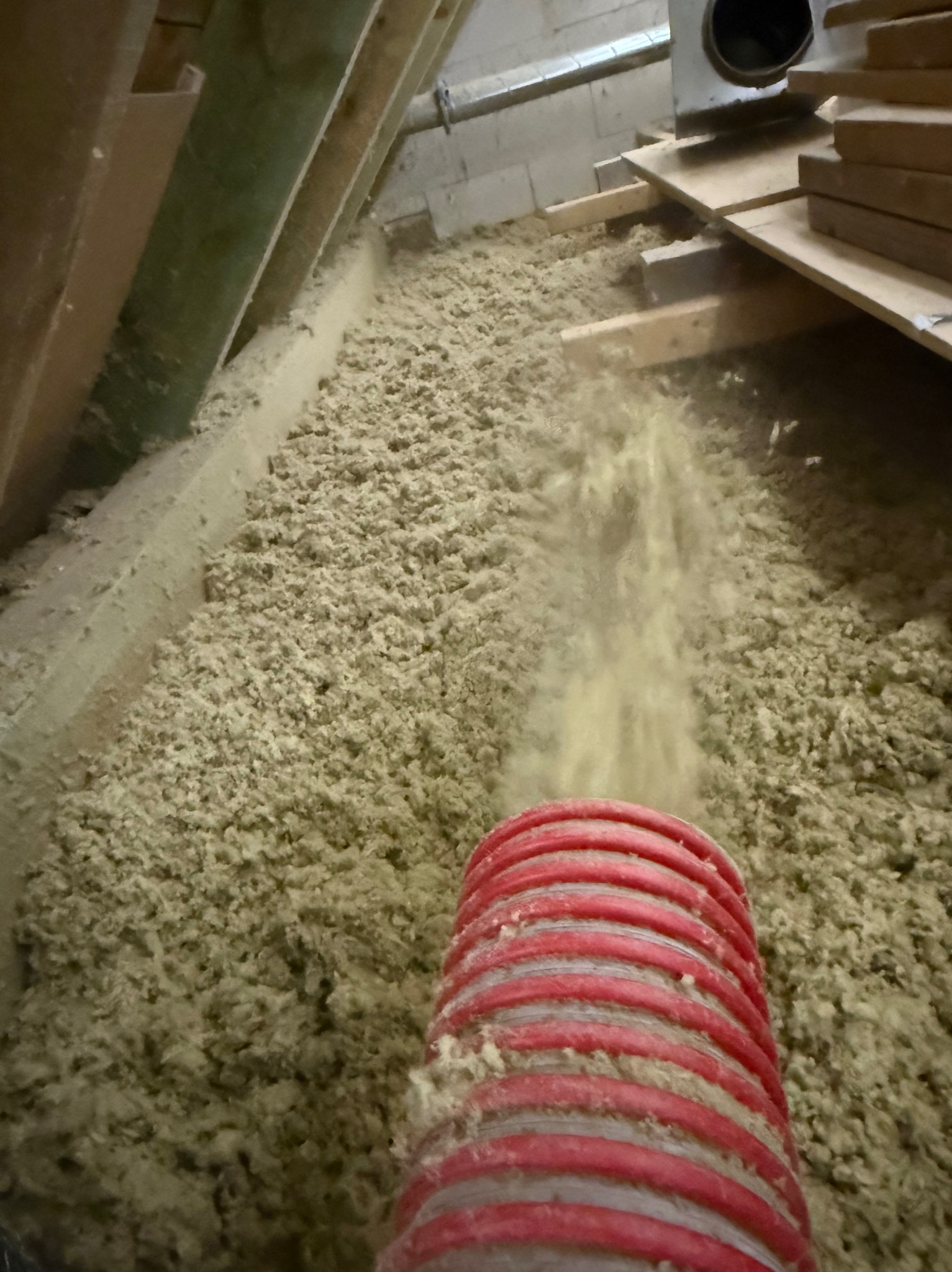 Aplikacja izolacji celulozowej na poddaszu za pomocą węża. Widoczne drewniane elementy konstrukcyjne i warstwa izolacji.