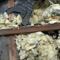 FURDREW Karol Furgała - Poddasze z widoczną izolacją z wełny mineralnej, częściowo zakryte czarną membraną dachową. Fragment czerwonej dachówki w prawym górnym rogu kadru.