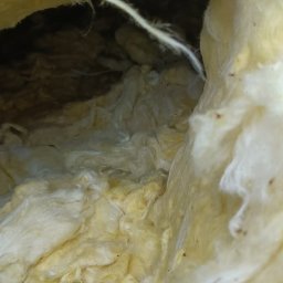 FURDREW Karol Furgała - Żółta wełna mineralna wypełniająca przestrzeń poddasza, widoczna z bliska, z ciemnym obszarem w tle. Izolacja termiczna poddasza.