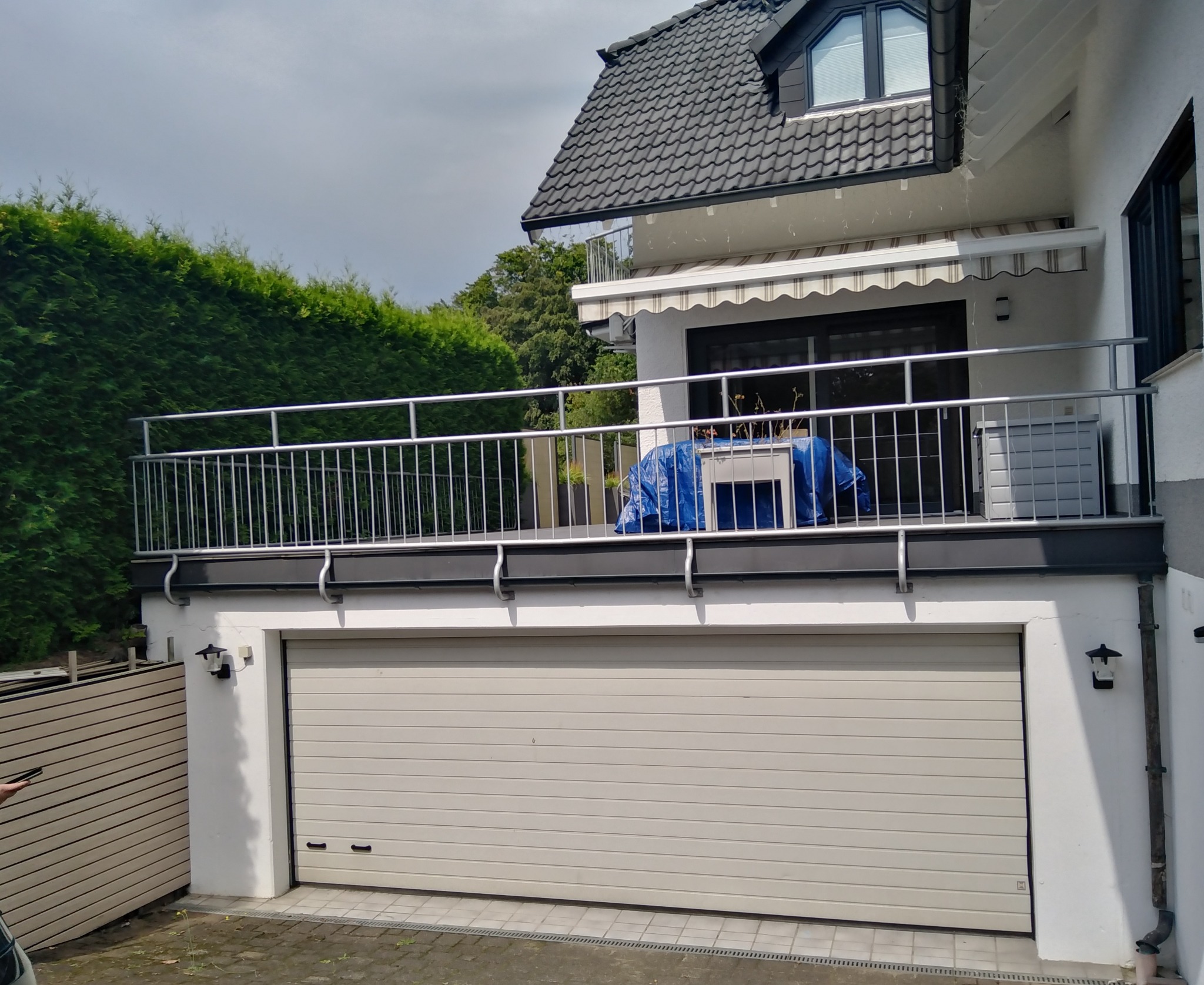 Zewnętrzna balustrada ze stali nierdzewnej na balkonie domu z garażem, widok z dołu na balkon z zewnątrz, elementy na balkonie zakryte plandeką.
