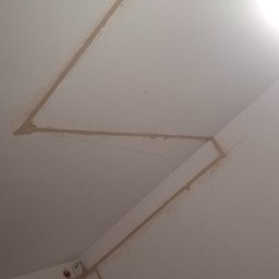 IHOR PARSHYKOV - Wykute w suficie i ścianie bruzdy pod kable elektryczne, widoczne kable wystające z sufitu i puszka elektryczna w rogu ściany.