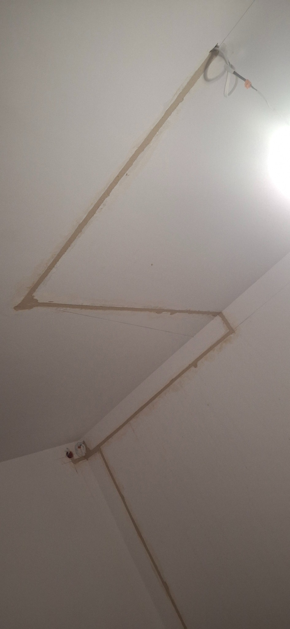 Wykute w suficie i ścianie bruzdy pod kable elektryczne, widoczne kable wystające z sufitu i puszka elektryczna w rogu ściany.