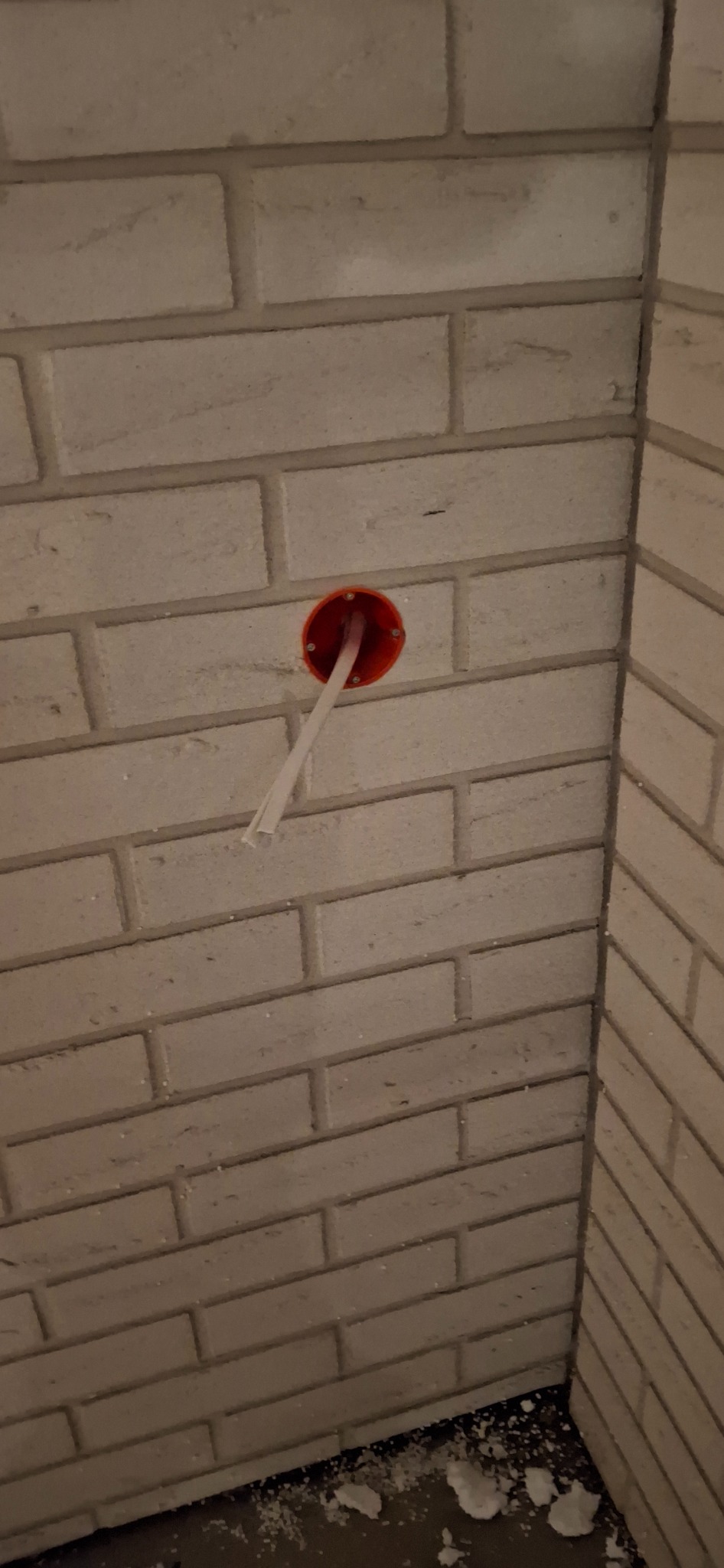 Czerwona puszka elektryczna w ścianie z cegły, z wystającymi kablami.