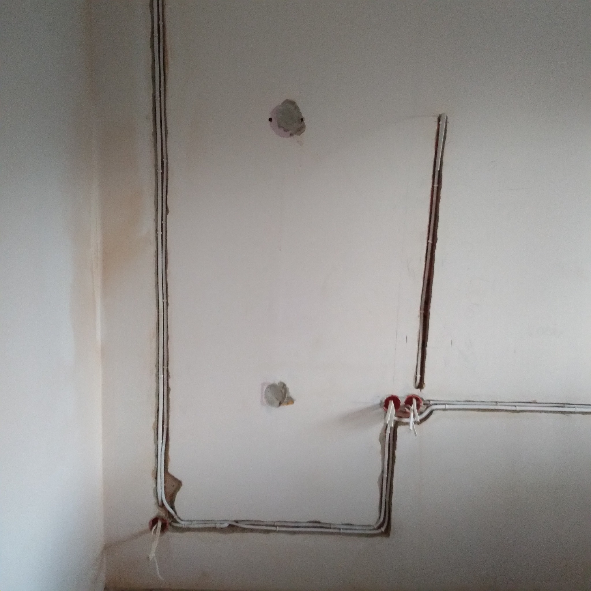 Świeżo położone kable elektryczne w bruzdach na ścianie, przygotowane do tynkowania, widoczne puszki instalacyjne z wystającymi przewodami.