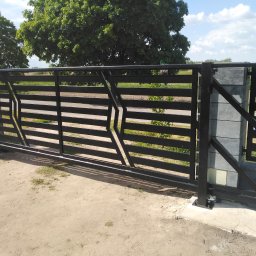 ART-SPAW - Czarna, przesuwna brama wjazdowa z poziomych profili, zamontowana w Rykach, z widocznym mechanizmem jezdnym i słupkami z szarej kostki.