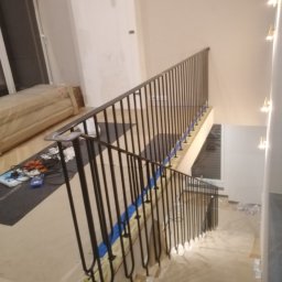 ART-SPAW - Montaż czarnej, metalowej balustrady schodowej w trakcie prac wykończeniowych. Zabezpieczone schody, widoczne narzędzia i materiały montażowe.