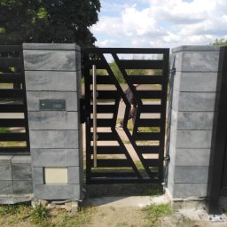 ART-SPAW - Nowoczesna brama wjazdowa z poziomymi przęsłami i geometrycznym wzorem, osadzona na szarych, betonowych słupkach z zamontowaną skrzynką na listy, widziana z perspektywy podwórza.