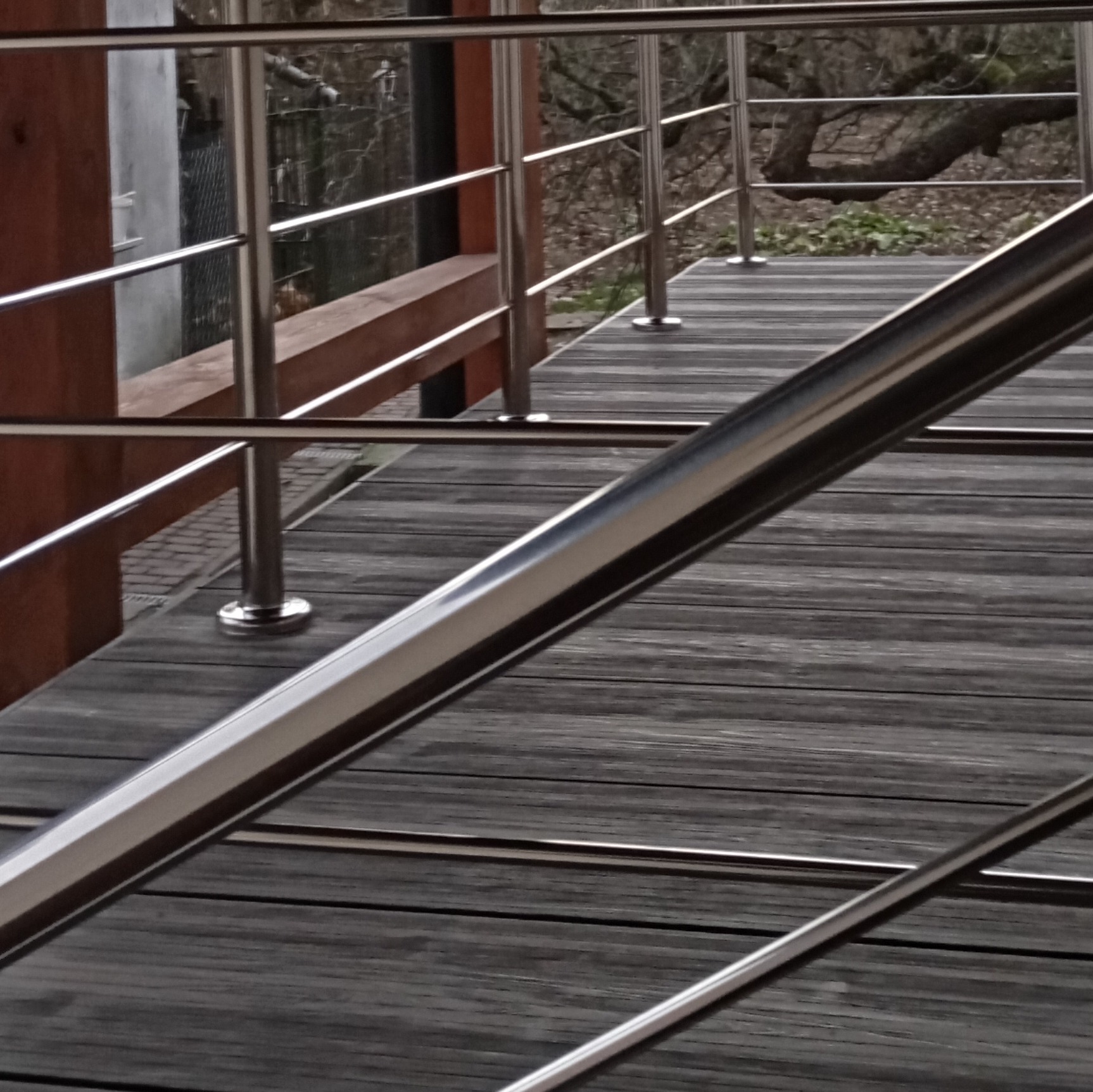 Metalowa balustrada z wypełnieniem linkami, zamontowana na drewnianym podeście, widok z dołu, z elementami otoczenia w tle.