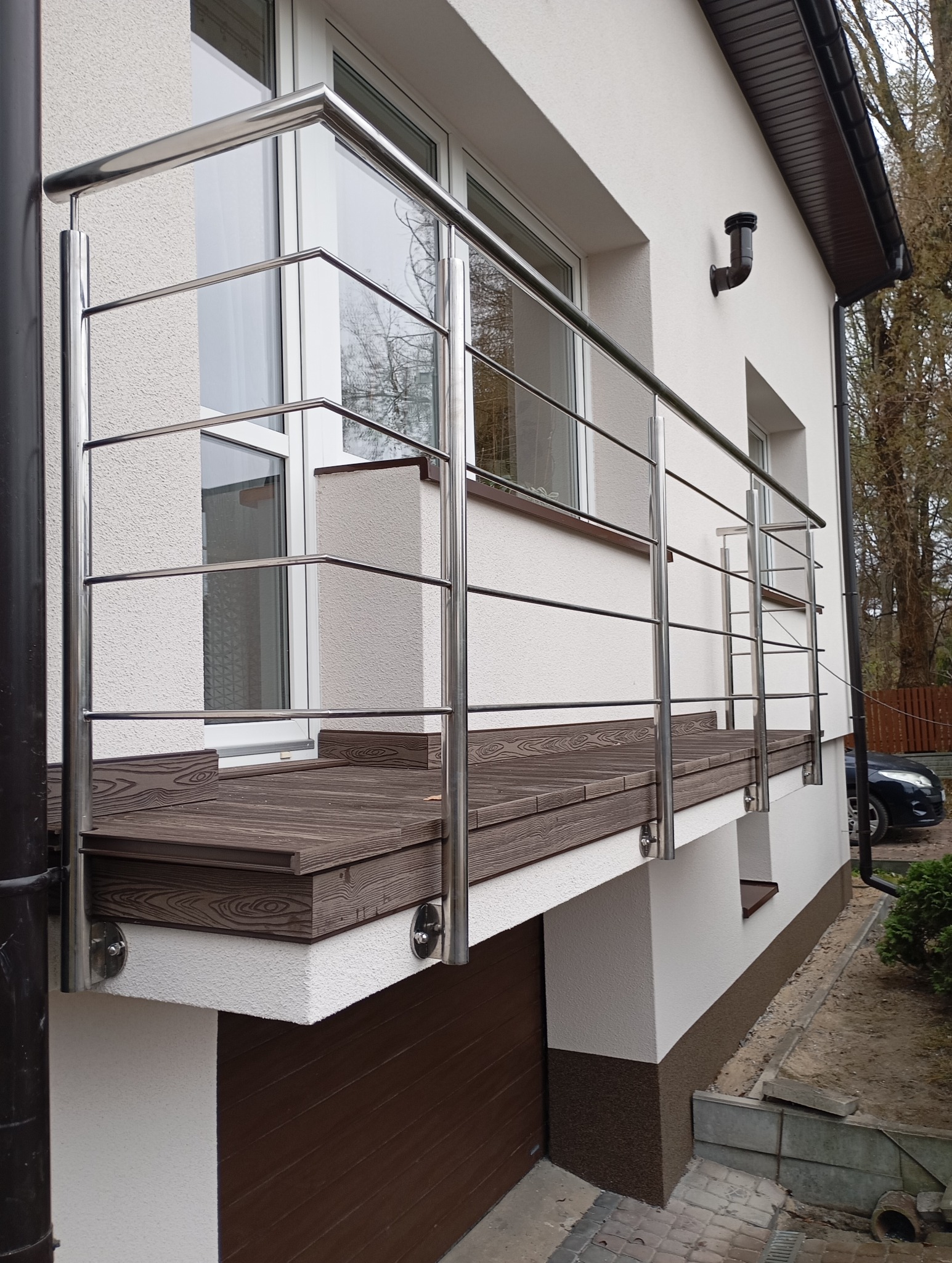 Balkon z podłogą z desek kompozytowych i nowoczesną balustradą ze stali nierdzewnej, mocowaną do ściany budynku.