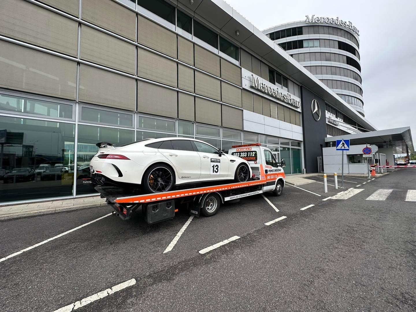 Biały Mercedes-Benz GT 63 S 4-Door Coupe z numerem 13 na lawecie pomocy drogowej przed salonem Mercedes-Benz.