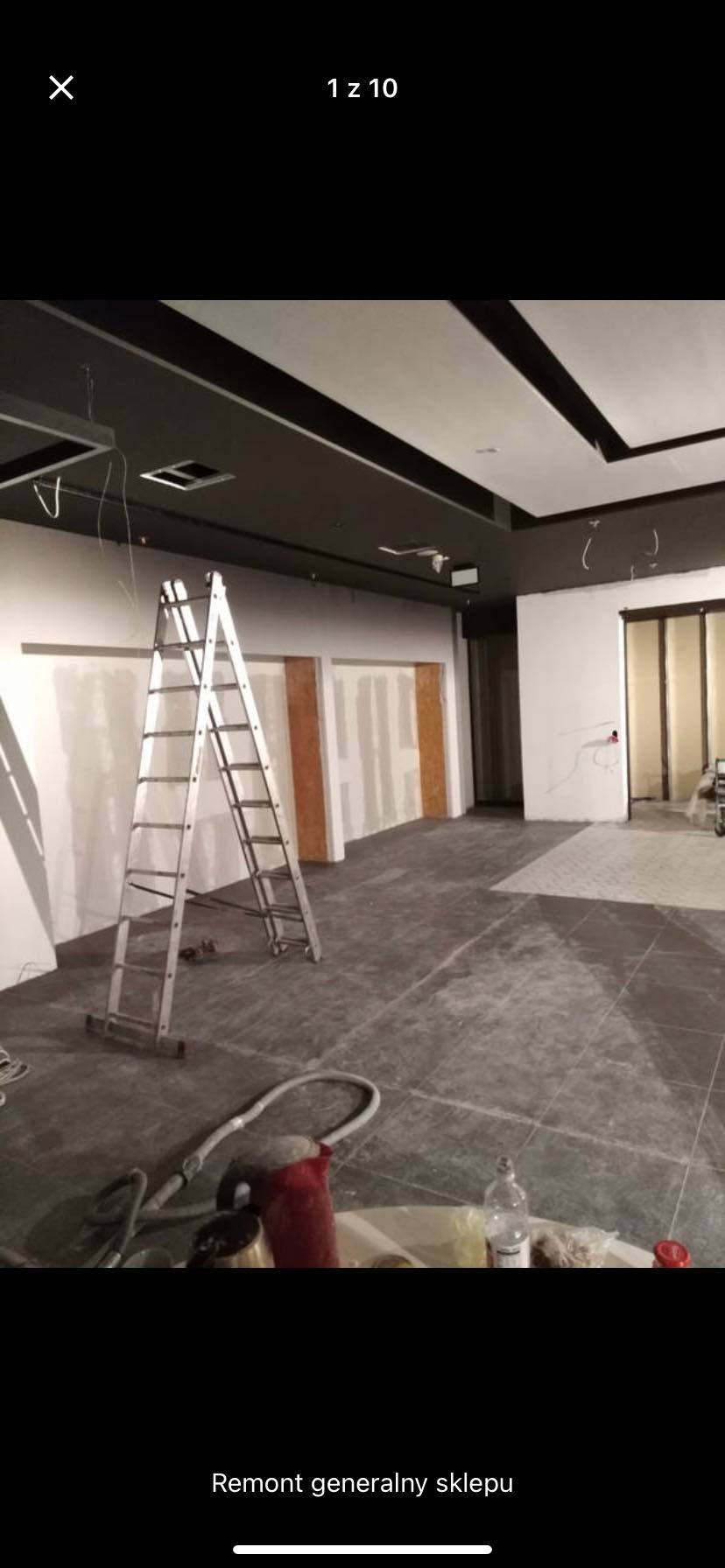 Wnętrze sklepu w trakcie remontu: widoczna drabina aluminiowa, częściowo wykończone ściany z płyt gipsowo-kartonowych, sufit z elementami dekoracyjnymi, oraz sprzęt budowlany na podłodze z szarych...