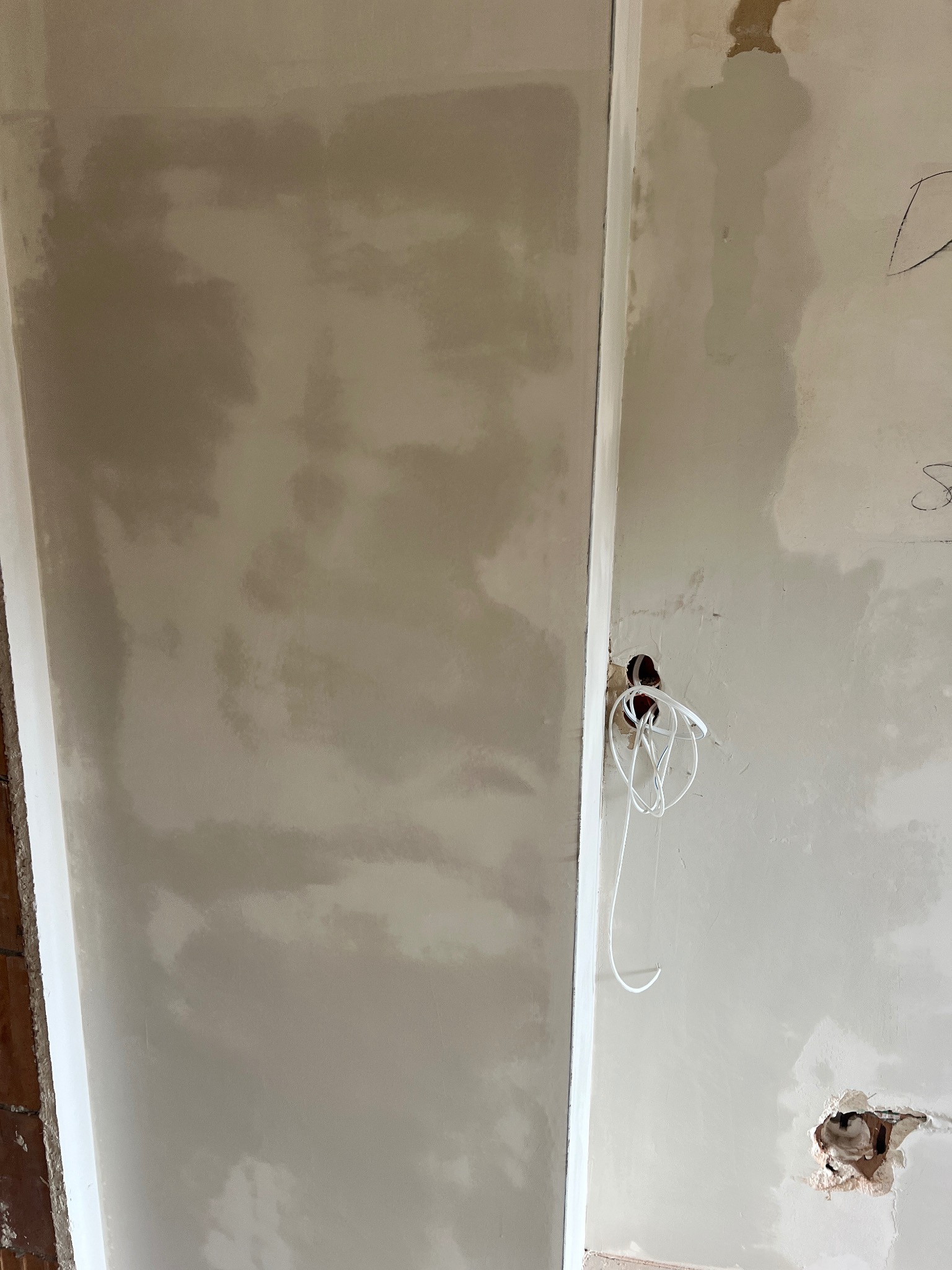 Świeżo położona gładź szpachlowa na ścianie, widoczne niedoskonałości i przygotowane otwory pod instalację elektryczną z wystającymi przewodami