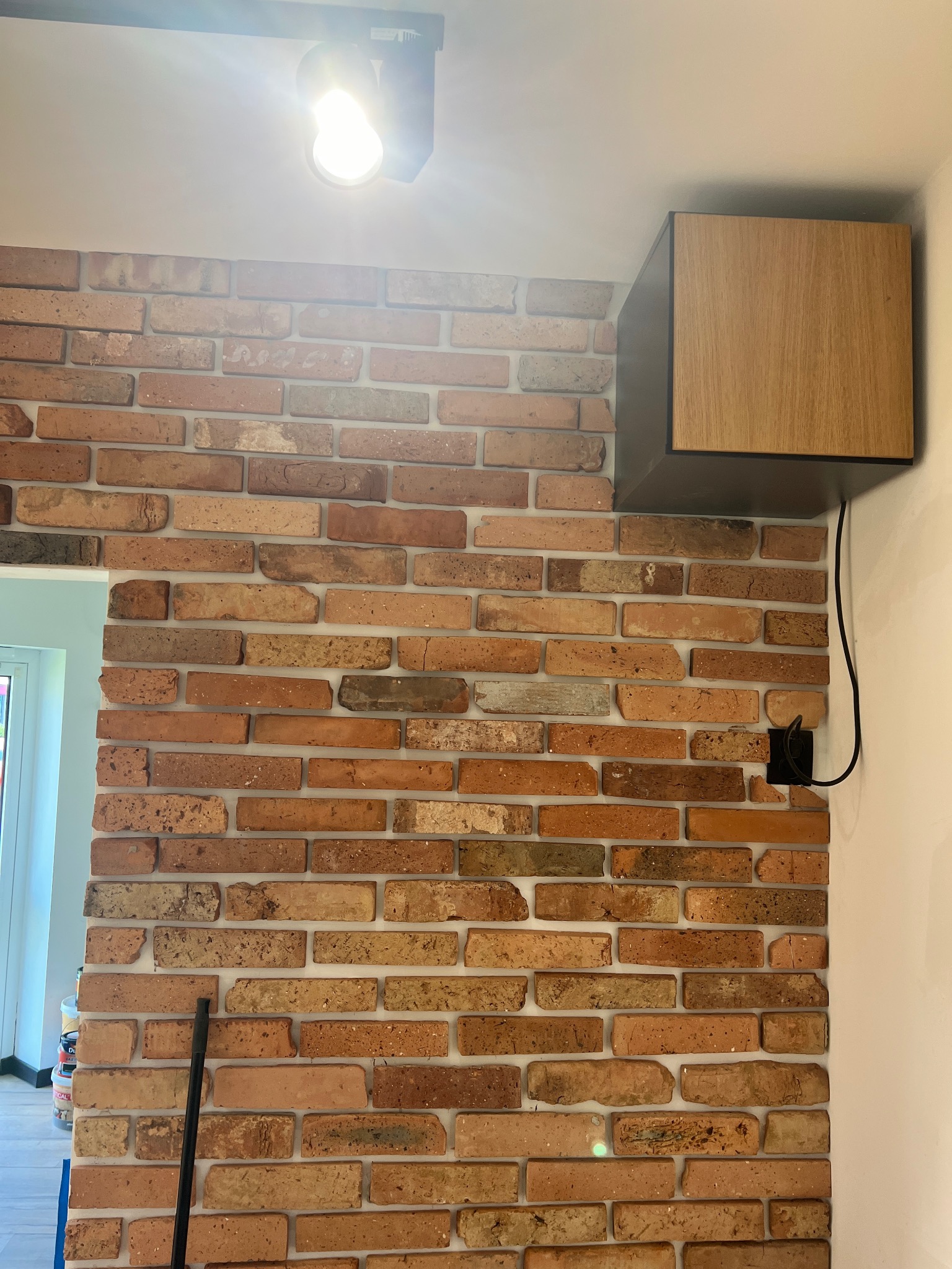 Dekoracyjna ściana z cegły klinkierowej w salonie, z wiszącą szafką z drewna i oświetleniem punktowym na suficie.