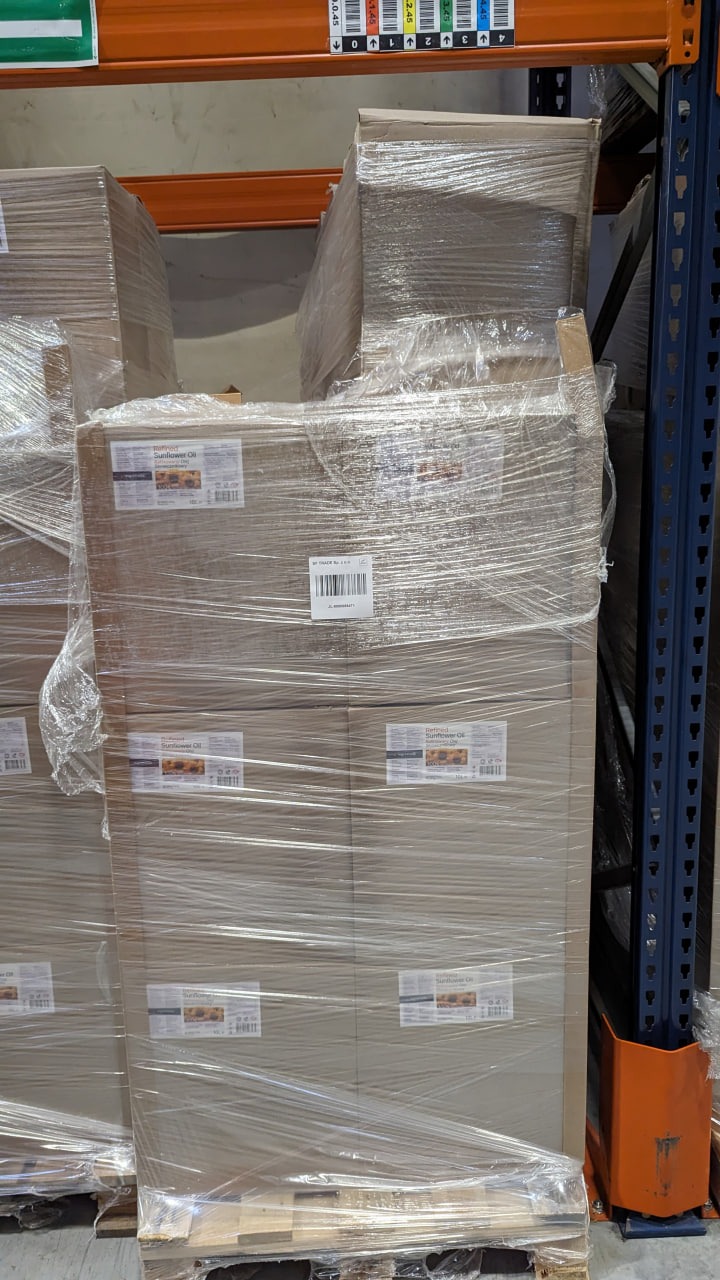 Paleta z kartonami oleju słonecznikowego, owinięta folią stretch, umieszczona na regale magazynowym.