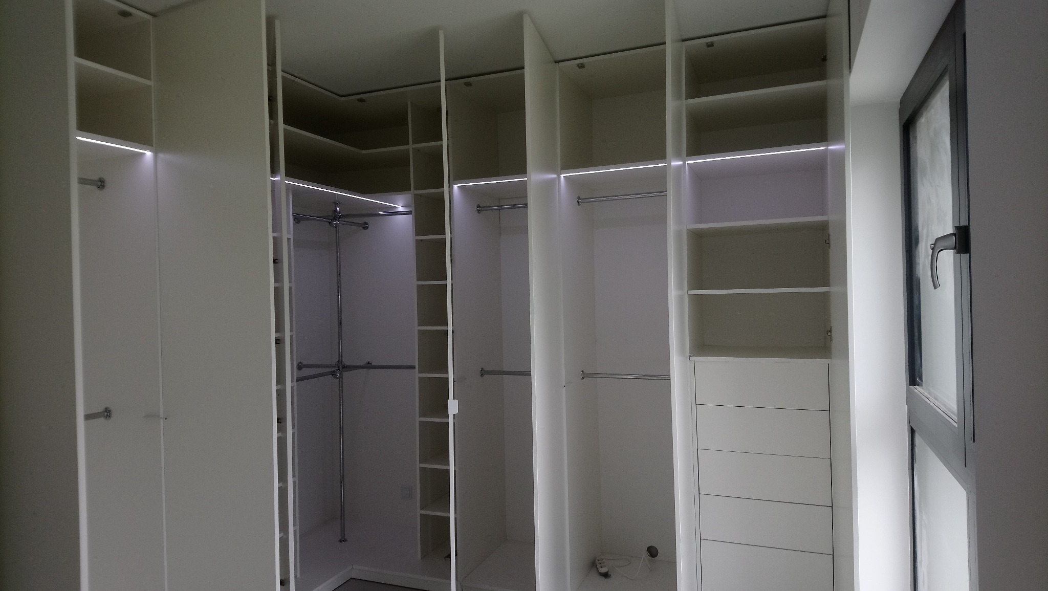 Wnętrze białej szafy wnękowej z oświetleniem LED, widoczne półki, drążki i szuflady, minimalistyczny design.