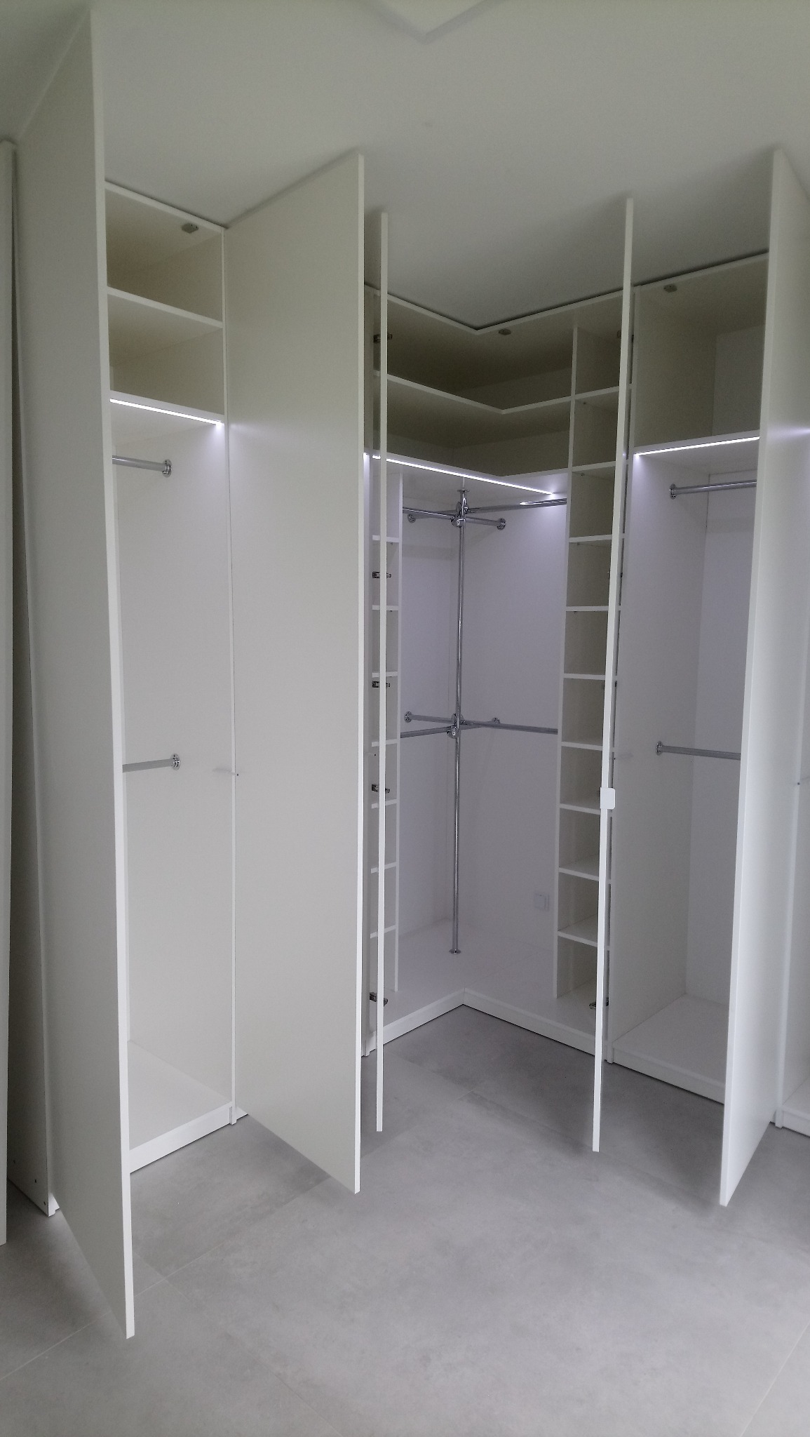 Biała, narożna szafa wnękowa z otwartymi drzwiami, oświetleniem LED i systemem drążków