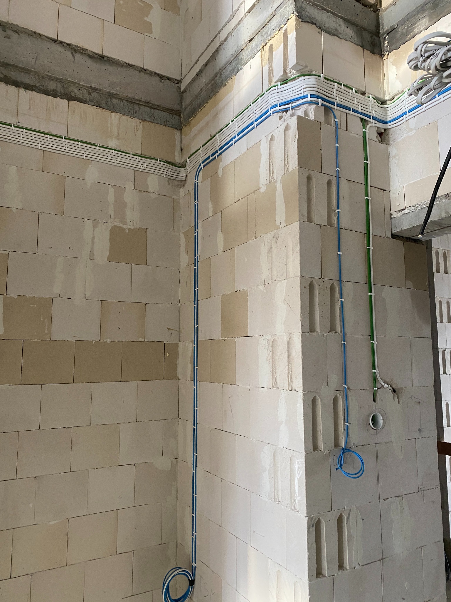Świeżo ułożone kable elektryczne w kolorowych peszlach, mocowane do surowych ścian z betonu komórkowego, widoczne puszki instalacyjne i fragmenty belek stropowych.