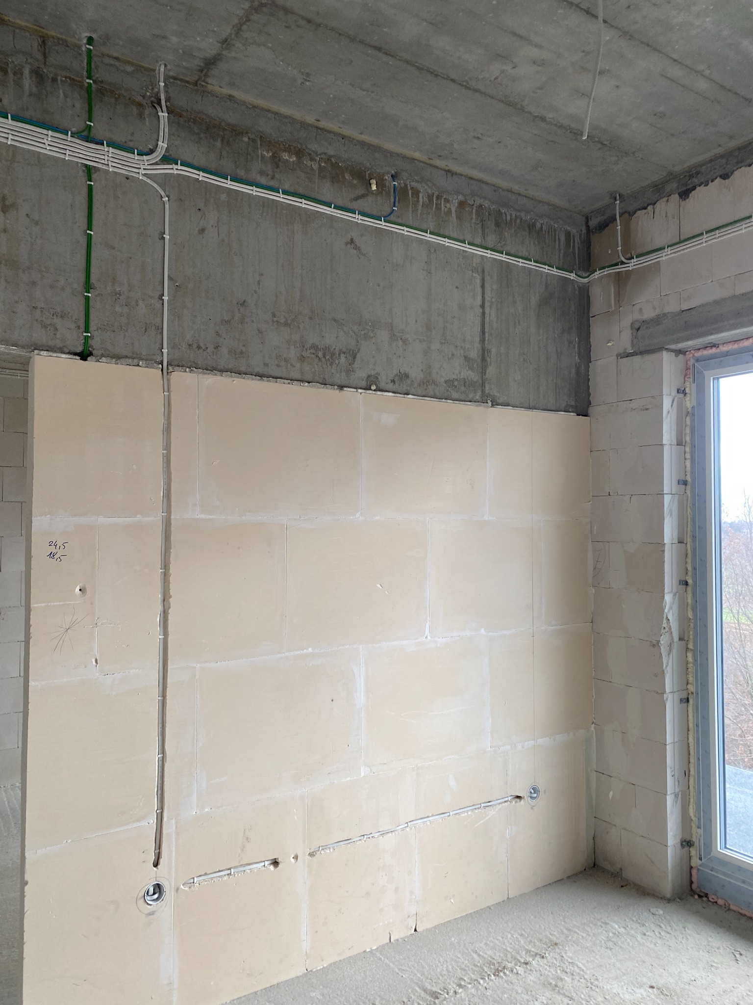 Surowy stan wnętrza z widocznymi przewodami elektrycznymi mocowanymi do ścian i sufitu, przygotowanymi do dalszych prac wykończeniowych.