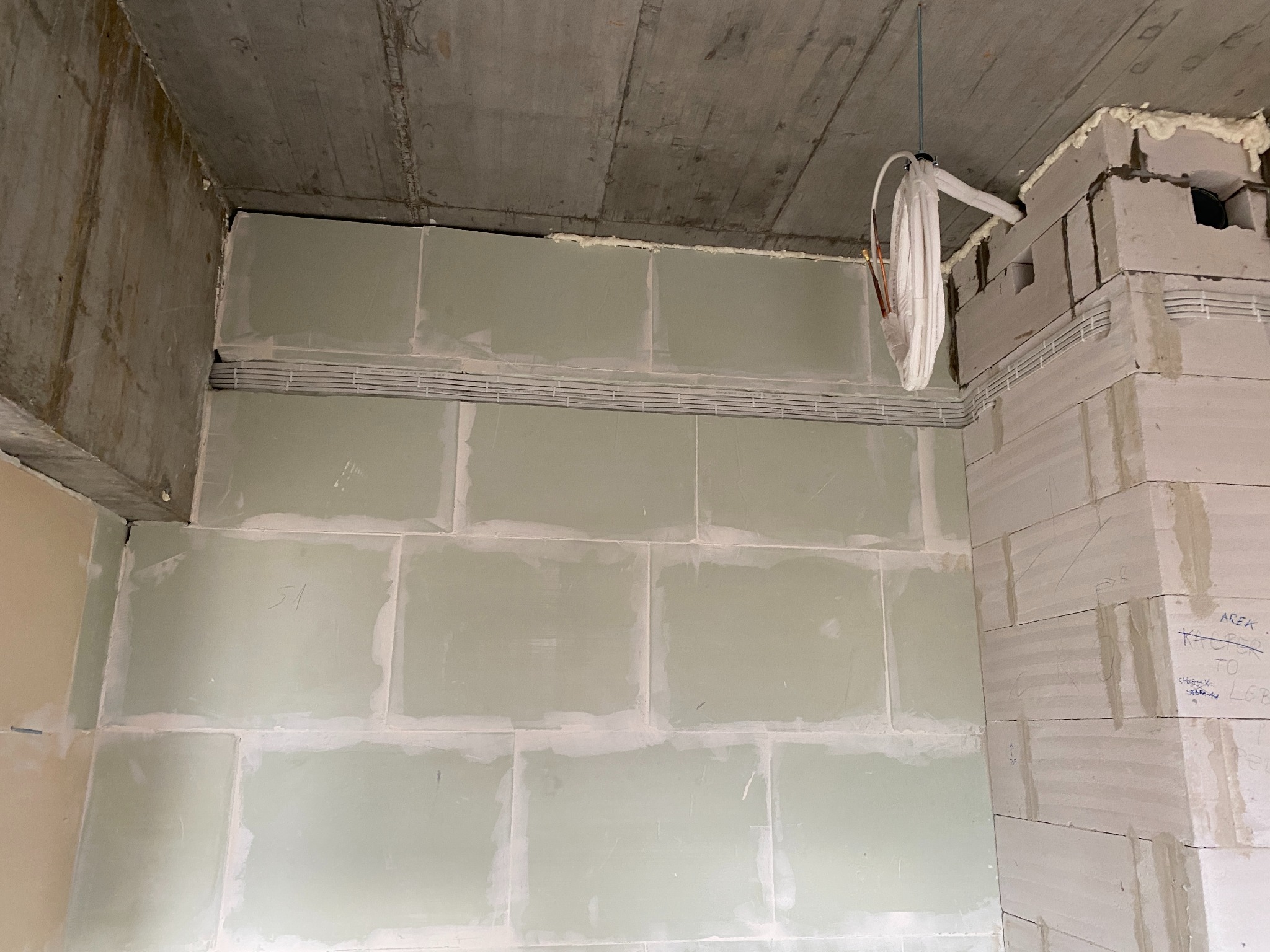 Wnętrze w trakcie wykańczania: ściany z bloków, przewody elektryczne w korytkach na ścianie, surowy betonowy strop, widoczne ślady po piance montażowej.