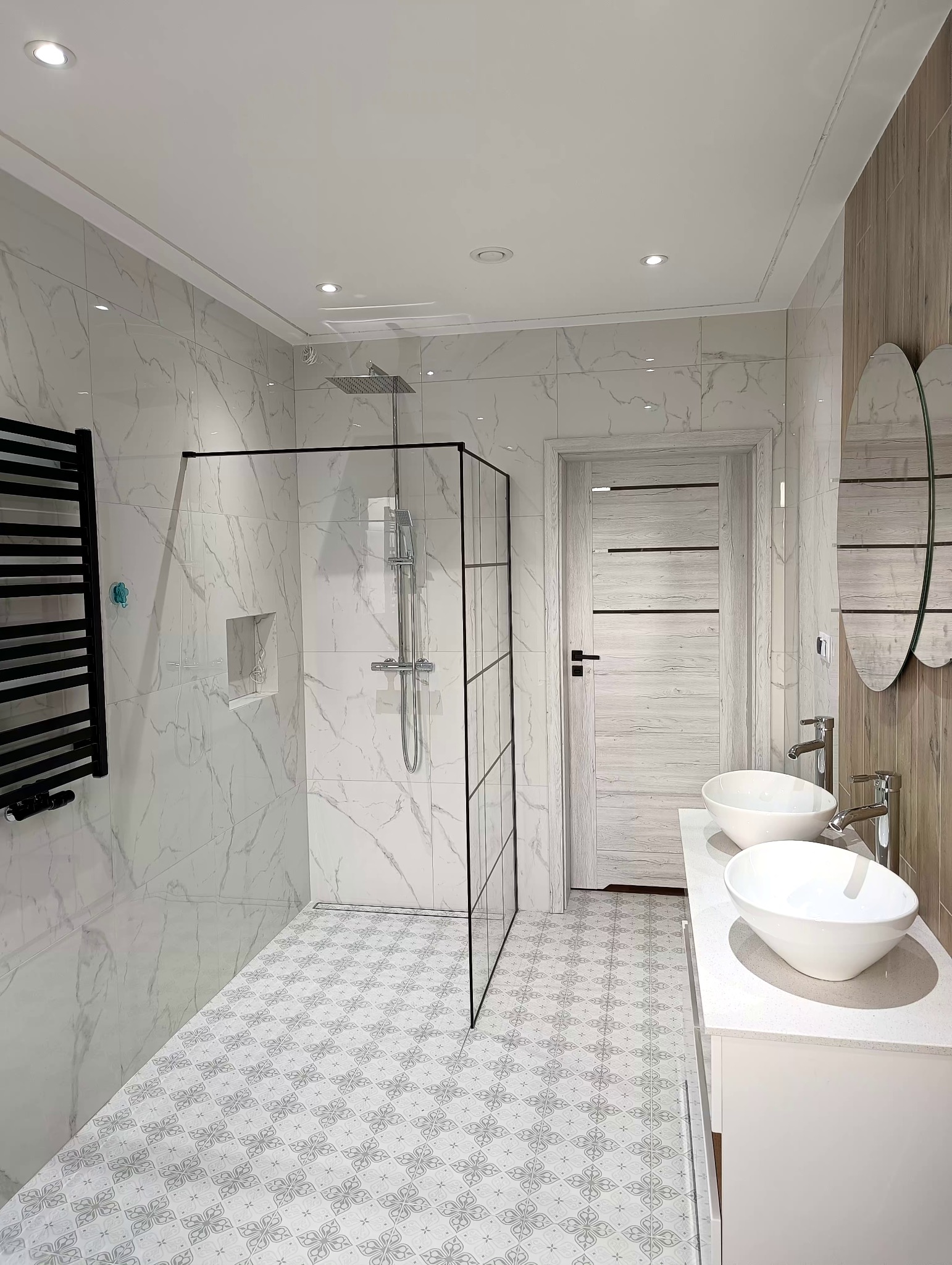 Nowoczesna łazienka z kabiną prysznicową typu walk-in, dwoma umywalkami nablatowymi i grzejnikiem drabinkowym w kolorze czarnym.