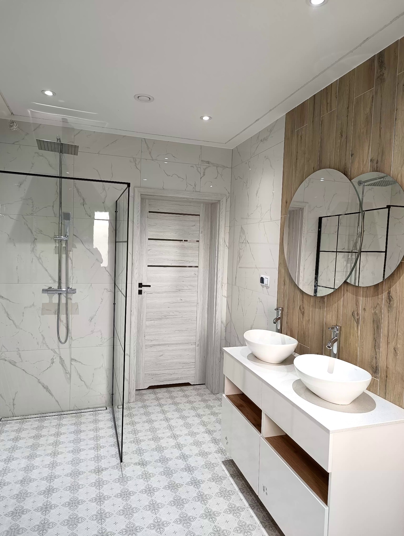 Nowoczesna łazienka z kabiną prysznicową typu walk-in, podwójną umywalką nablatową i płytkami imitującymi marmur oraz drewno.