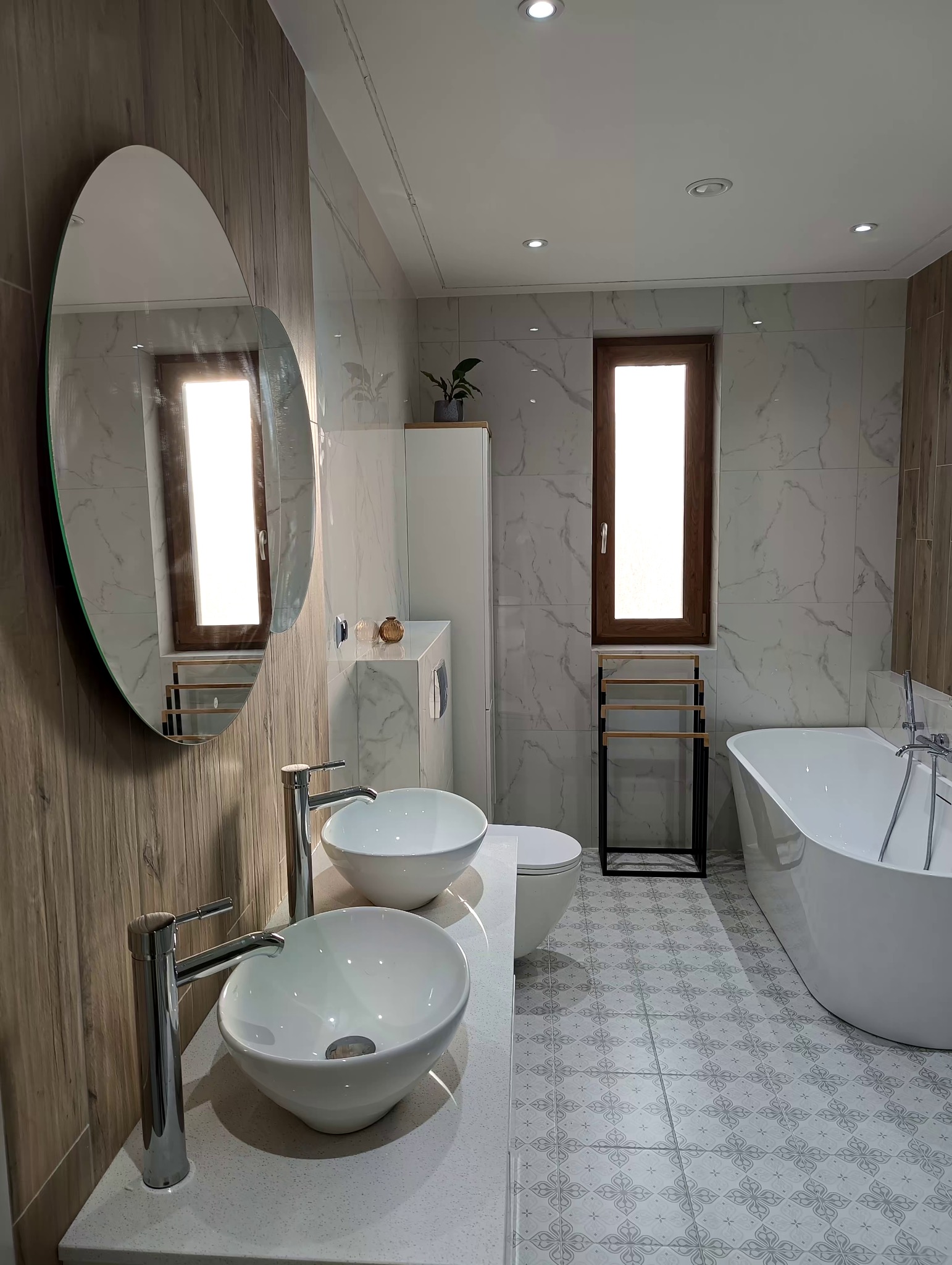 Jasna łazienka z dwoma umywalkami nablatowymi, okrągłym lustrem, wanną wolnostojącą i płytkami podłogowymi we wzory.