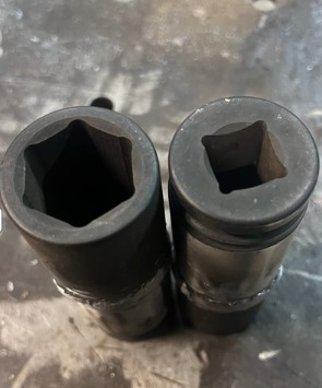 Dwie nasadki udarowe, jedna sześciokątna, druga kwadratowa, ustawione pionowo na metalowej powierzchni z widocznymi śladami użytkowania i spawania.