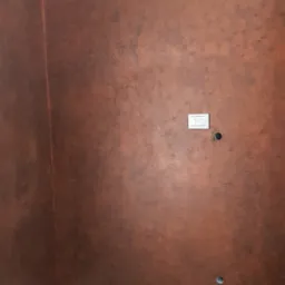 Ściana w kolorze miedzi z efektem patyny, listwa przypodłogowa w kolorze białym, gniazdka elektryczne i otwory na kable, sufit z oświetleniem punktowym, podłoga wyłożona panelami.