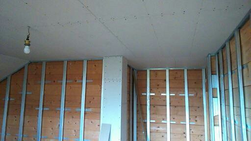 Wnętrze w trakcie prac wykończeniowych: drewniane ściany z metalową konstrukcją, sufit z płyt kartonowo-gipsowych, wisząca żarówka.