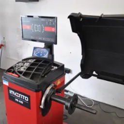 Wyważarka do kół Invento VB 470 z ekranem i osłoną, widoczna w warsztacie samochodowym, gotowa do użycia. Na ekranie widoczne parametry ustawień.