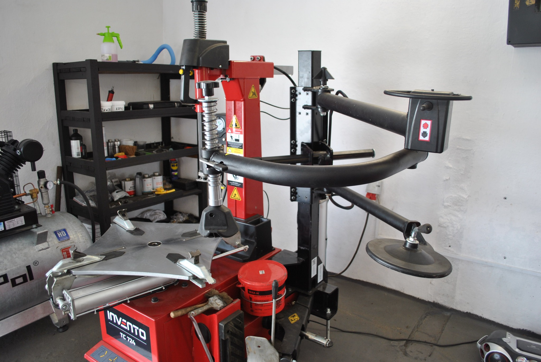 Wyważarka do opon Invento TC 724 w warsztacie samochodowym, widoczny kompresor i półki z narzędziami w tle.