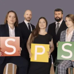 Pięcioosobowa grupa w formalnych strojach trzyma kolorowe kwadraty z literami S, P, S, tworząc skrót nazwy firmy lub idei.