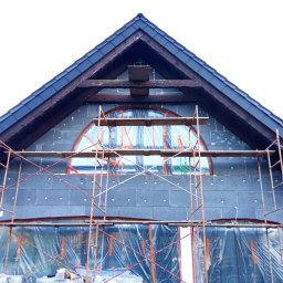 ROBI-HOME Posadzki Żywice Kamienny Dywan - Budynek w trakcie ocieplania styropianem grafitowym, zabezpieczony folią i rusztowaniem, widoczne drewniane elementy konstrukcyjne dachu.