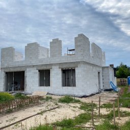 Bohdan Kostiuchyk Dream House - Wznoszenie ścian parterowego domu z białych bloczków, widoczna konstrukcja zbrojeniowa na gruncie i przenośna toaleta w tle.