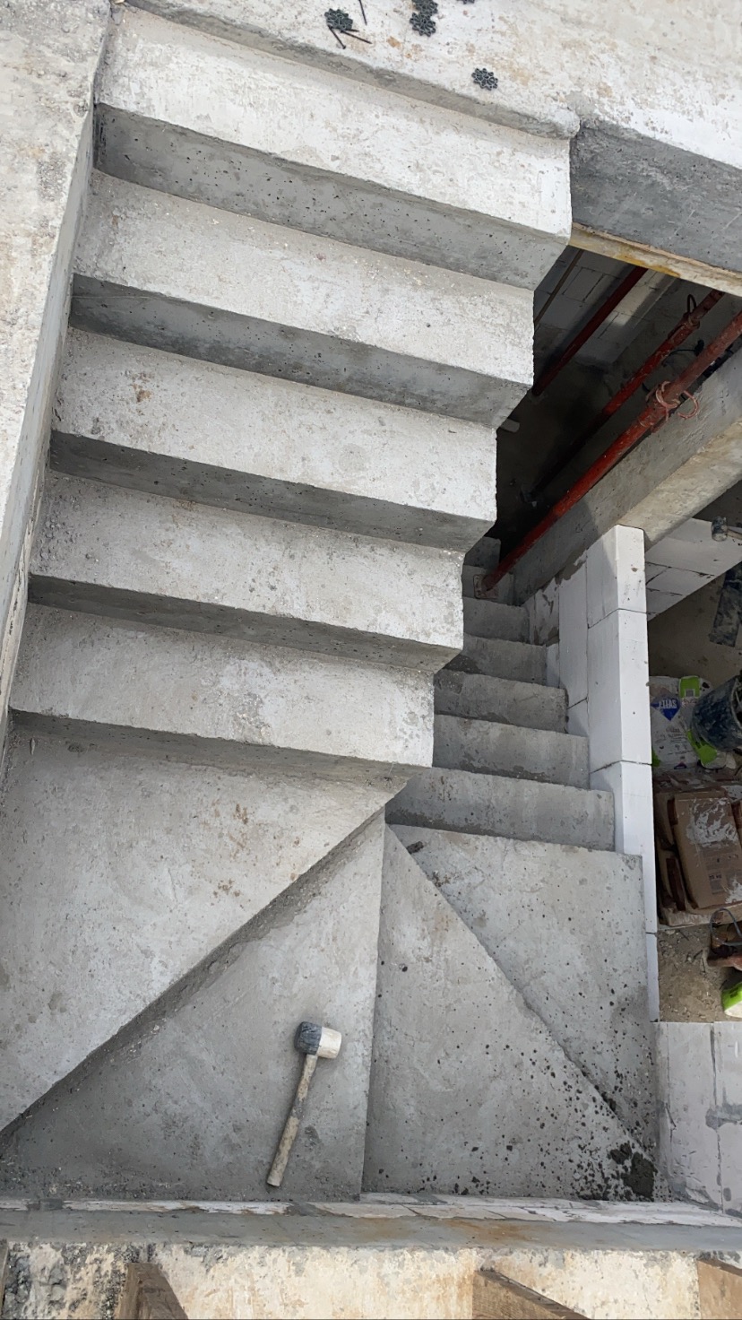 Surowe betonowe schody wewnętrzne w trakcie budowy, widok z góry, z gumowym młotkiem leżącym na dolnym stopniu.