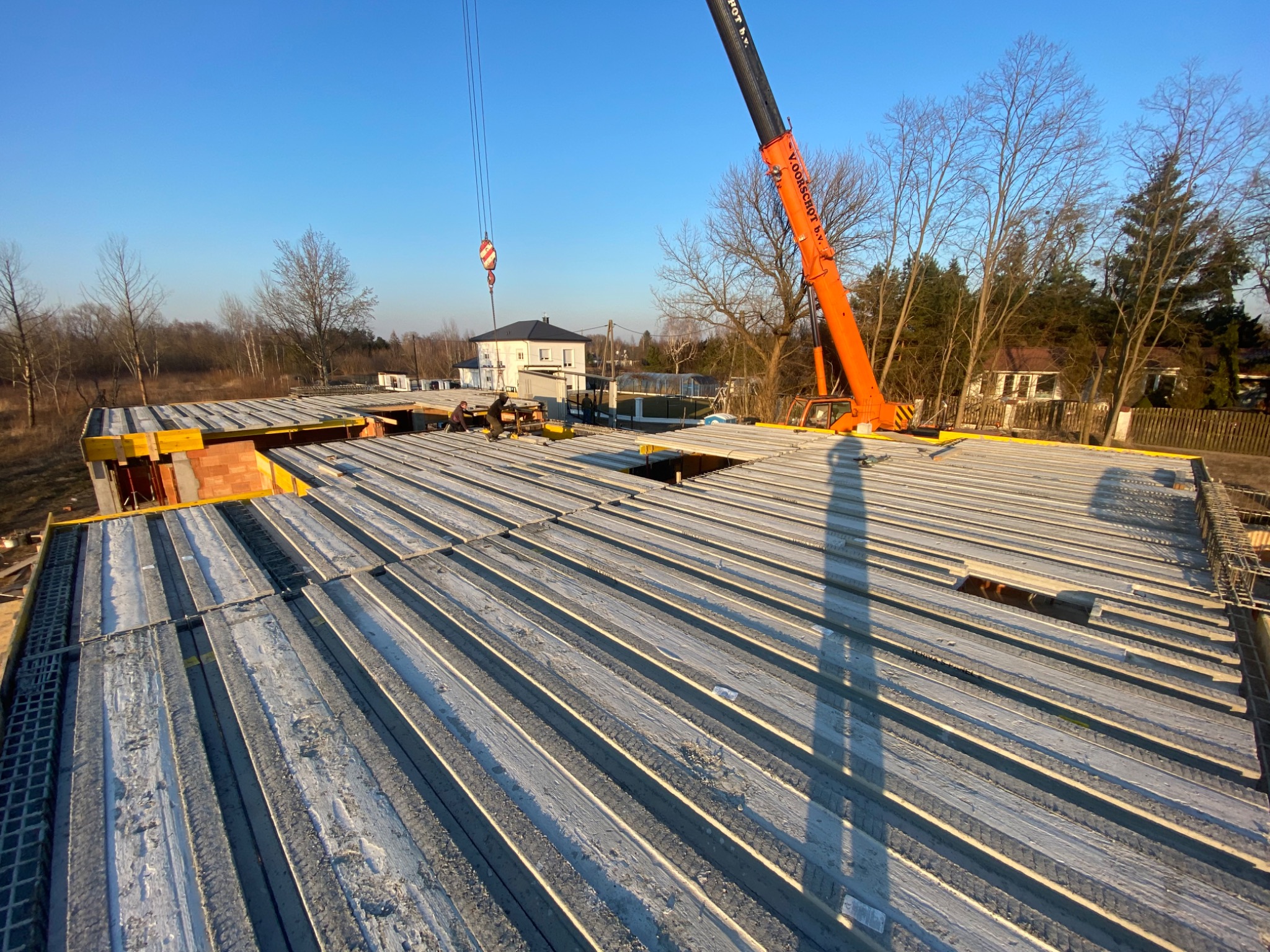 Montaż stropu Teriva na budowie domu jednorodzinnego z użyciem dźwigu, widoczne pustaki ceramiczne i zbrojenie.