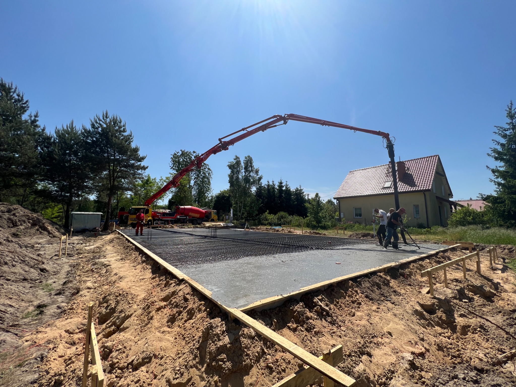 Wylewanie betonu na przygotowany fundament zbrojony w Warszawie, widoczny betonowóz z pompą i pracownicy wygładzający powierzchnię.