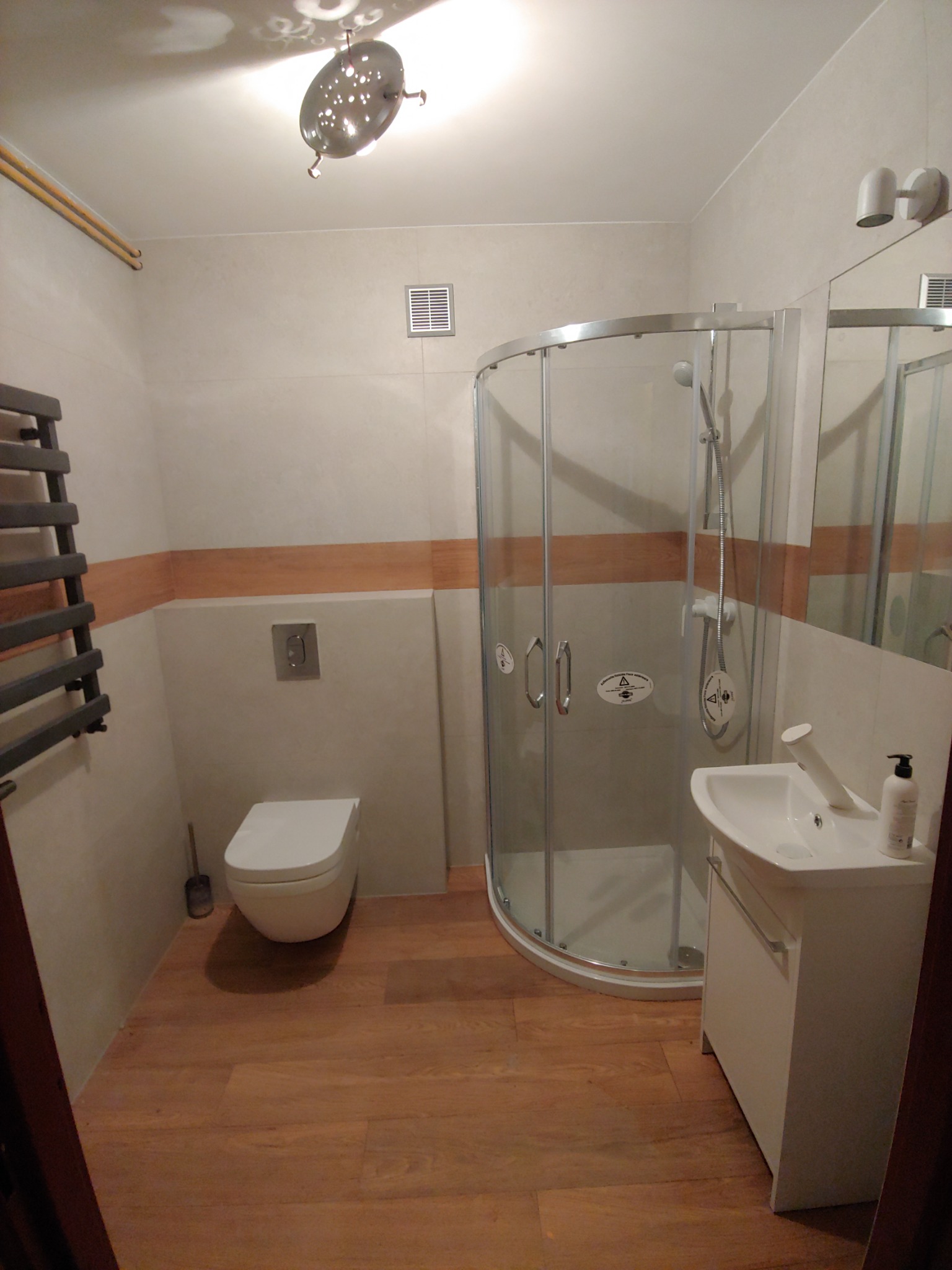 Wykończona łazienka w Biłgoraju z drewnopodobną podłogą, kabiną prysznicową z zaokrąglonymi drzwiami, podwieszaną toaletą i grzejnikiem drabinkowym.