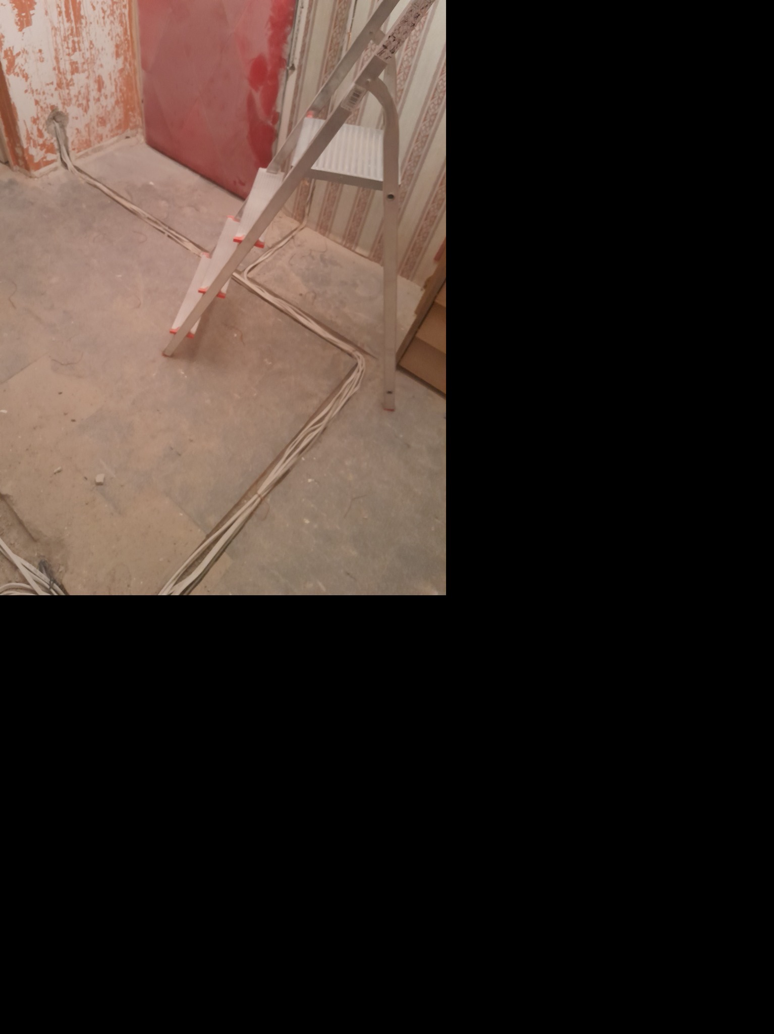 Wnętrze w trakcie prac: widoczne przewody elektryczne ułożone na podłodze, drabina aluminiowa, ściany w stanie surowym i częściowo z tapetą.