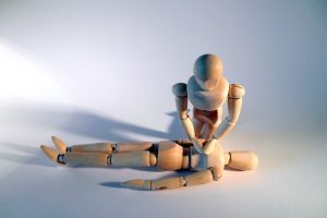 Manekin drewniany demonstrujący resuscytację krążeniowo-oddechową, dłonie ułożone na klatce piersiowej, ułożony na jasnym tle.