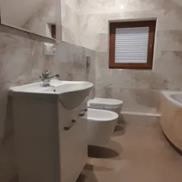 Wykończona łazienka na poddaszu ze skośnym sufitem, z umywalką z szafką w kolorze białym, toaletą, bidetem i oknem z drewnianą ramą oraz żaluzjami plisowanymi.