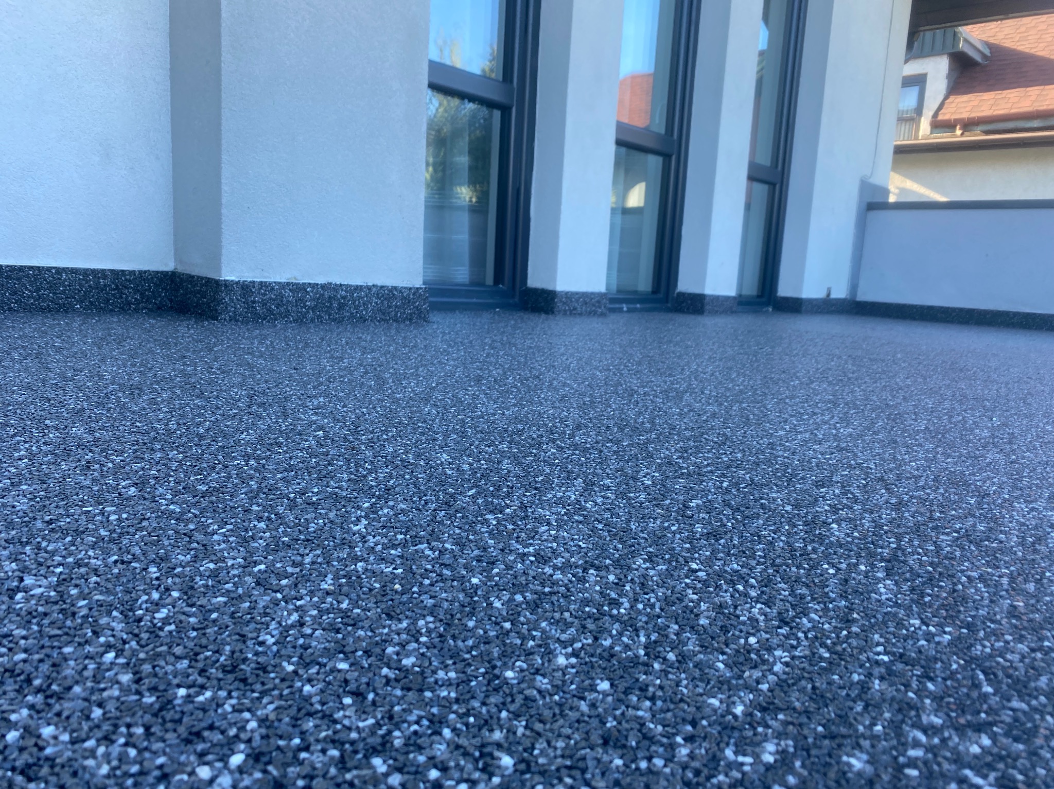 Wykończony balkon z posadzką typu kamienny dywan w odcieniach szarości i bieli, widok z niskiego kąta, z fragmentem elewacji budynku i okien.