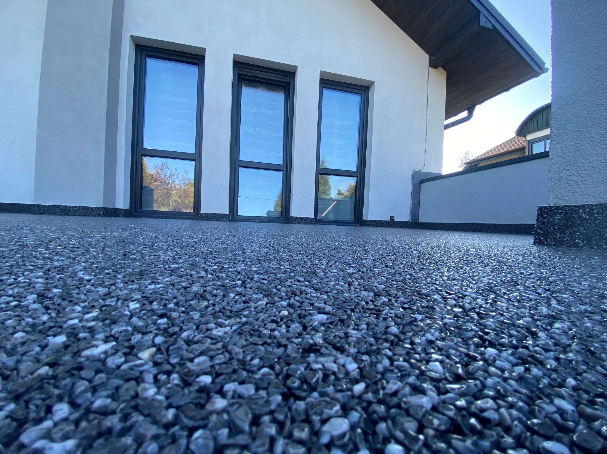 Szary kamienny dywan na tarasie z trzema oknami w tle, widok z niskiej perspektywy.
