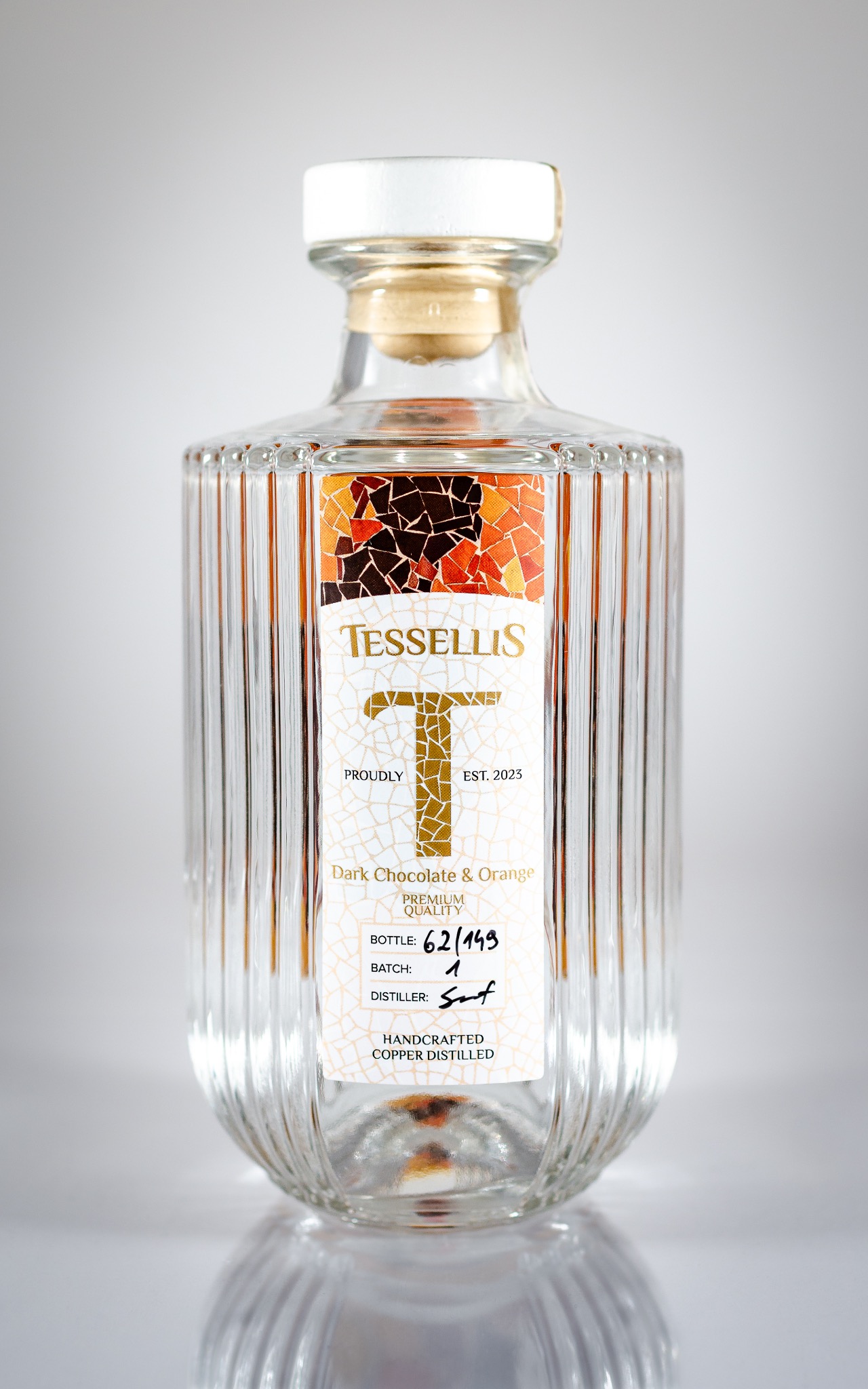 Elegancka, przezroczysta butelka wódki Tessellis Dark Chocolate & Orange z korkiem, z mosaic-owym wzorem na etykiecie, numerowana partia 62/149, destylowana w miedzianym alembiku.