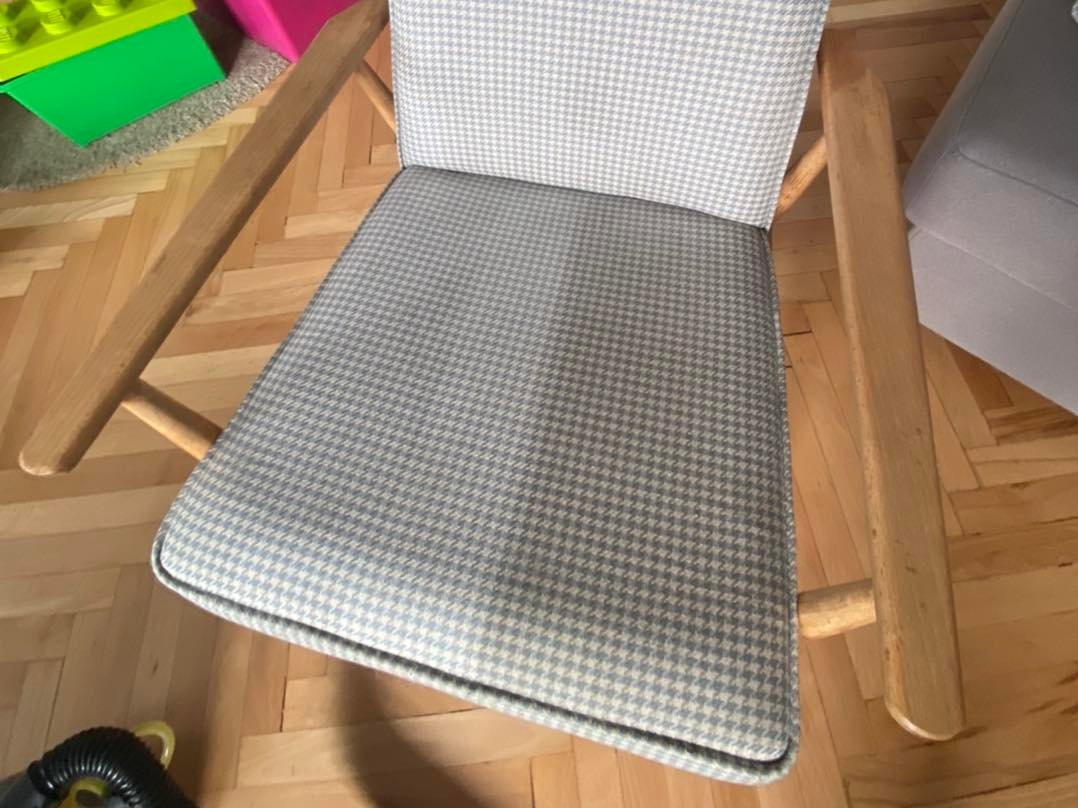 Drewniane krzesło z tapicerką w pepitkę, widoczne na parkiecie, obok zabawki i odkurzacz.