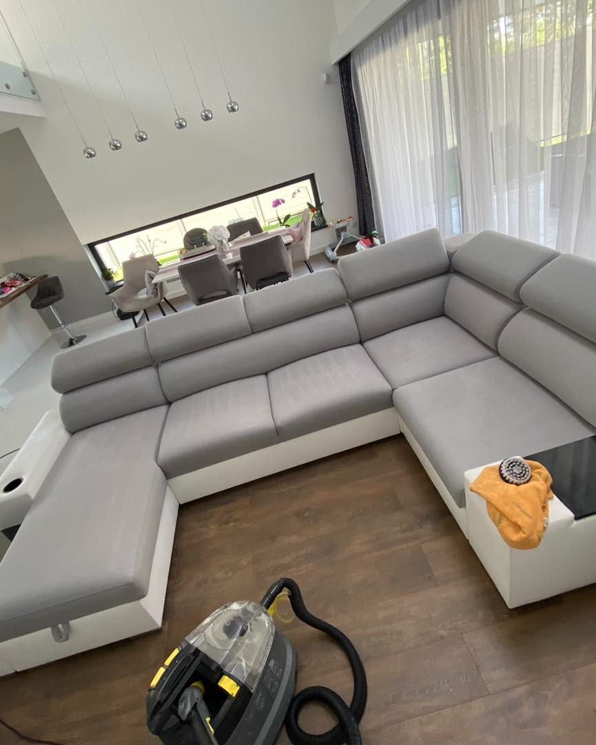 Szary, modułowy narożnik z białymi bokami w przestronnym salonie, obok leży odkurzacz piorący i żółta ściereczka, widoczne ślady czyszczenia.