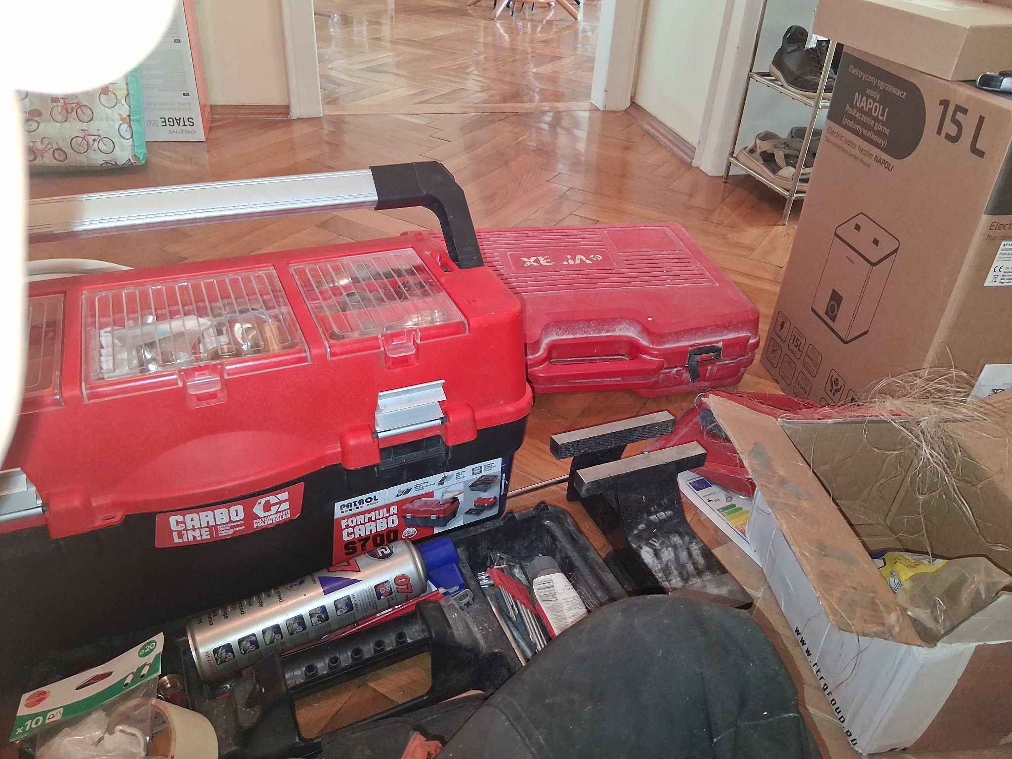 Skrzynka narzędziowa Patrol Carbo 5700 i pudełko z grzejnikiem Napoli 15L na podłodze w Bielsku-Białej. Widoczne narzędzia i akcesoria instalacyjne.