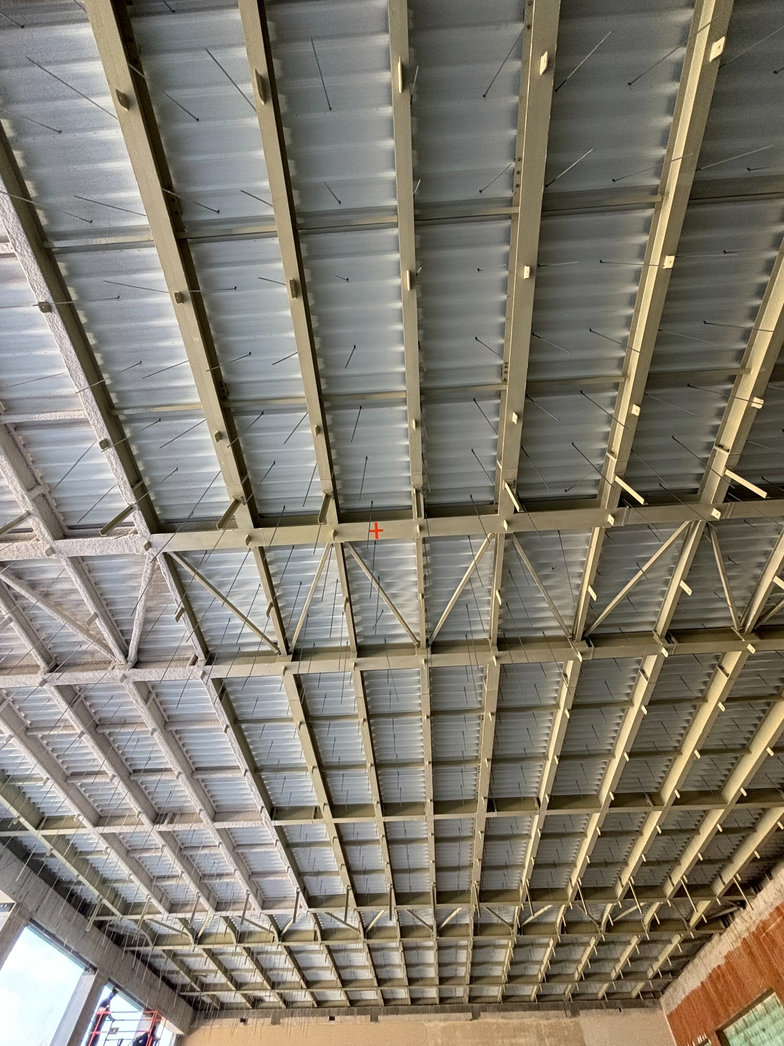 Widok z dołu na konstrukcję stalową dachu hali w trakcie budowy, widoczne elementy mocujące i izolacja.
